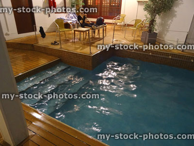 Stock image of teenage boy sitting, rectangular indoor swimming pool, wooden floor