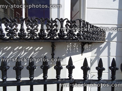 Stock image of ornate black iron railings against bay window / white wall
