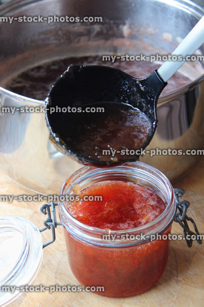 Stock image of hot strawberry jam being ladled into sterilised glass jam jars