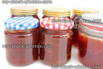 Stock image of homemade plum and strawberry jam in glass jars, metal clip, screw lids