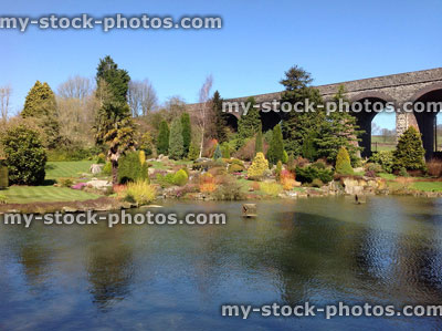 Stock image of pond with yellow water lily flowers, rockery, rock garden, aqueduct bridge