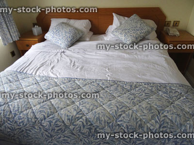 Stock image of large king size double bed with quilt cover, cushions, wooden headboard