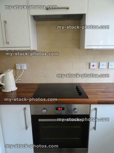 Stock image of modern glossy white kitchen cabinets / wall cupboards, wooden laminate worktop, hob, fitted oven