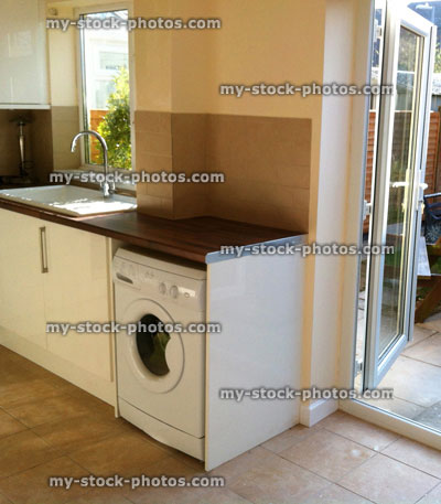 Stock image of modern kitchen diner, glossy white cupboards, washing machine, ceramic kitchen sink, patio doors