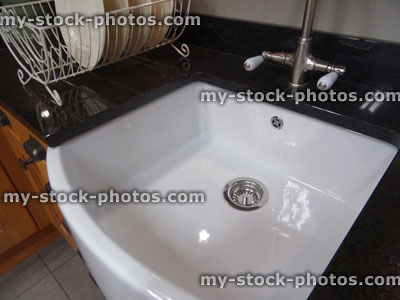 Stock image of traditional kitchen, black granite worktop counter, white ceramic Belfast / Butler sink