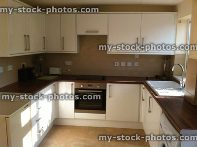 Stock image of modern kitchen with white glossy cabinets, cooker, sink, wooden worktops