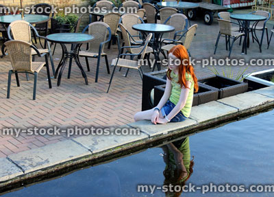 Stock image of girl by large koi carp pond, with reflection in water
