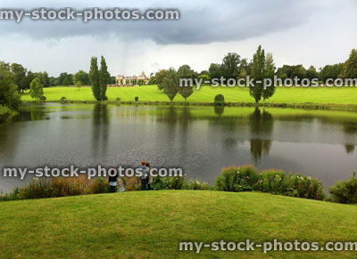 Stock image of family by large lake with green lawn and storm clouds