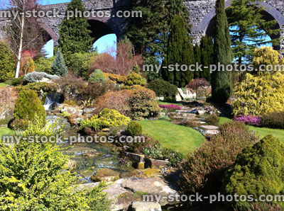 Stock image of cascading waterfall in rockery garden, dwarf conifers, bridge