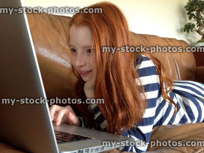 Stock image of girl lying on sofa using silver MacBook laptop