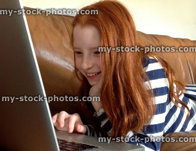 Stock image of girl using Apple laptop computer lying on leather sofa