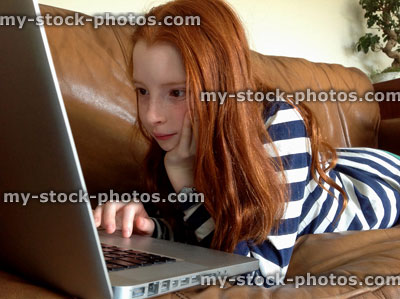 Stock image of girl lying on sofa looking a laptop screen