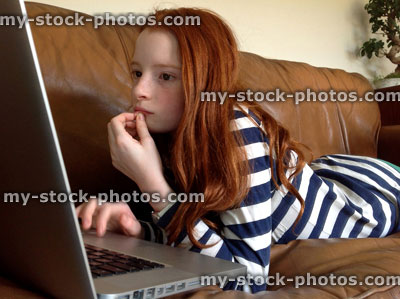 Stock image of girl looking at website on laptop screen, lying down