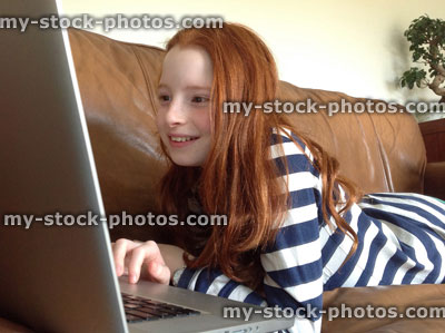 Stock image of girl using a laptop computer while lying on sofa