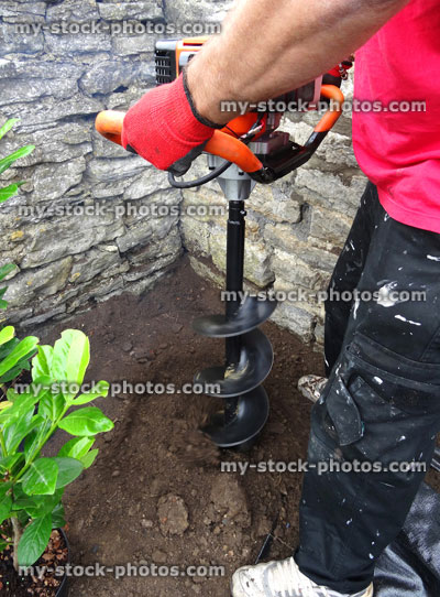 Stock image of petrol corkscrew fence digger / auger tool digging hole, planting laurel hedge