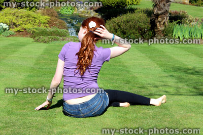 Stock image of red haired girl sitting on manicured lawn with pony tail 