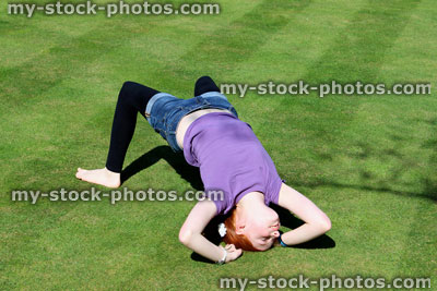 Stock image of red haired girl posing in bridge position on manicured lawn