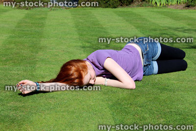 Stock image of red haired girl lying stretched out on a manicured lawn 