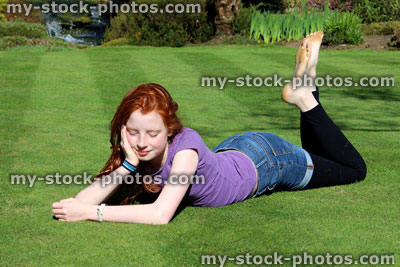 Stock image of red haired girl lying stretched out on a manicured lawn 