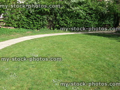 Stock image of large round garden lawn with daisies, curving pathway
