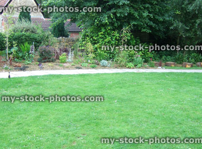 Stock image of large garden lawn with paved footpath, planted flowerbed