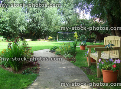 Stock image of concrete pathway through shady garden, wooden bench seat
