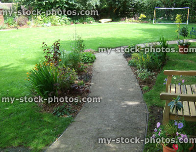 Stock image of shady garden with flowers, wooden bench, concrete path