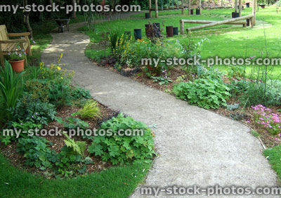 Stock image of shady garden, herbaceous flowers, wooden bench, concrete path