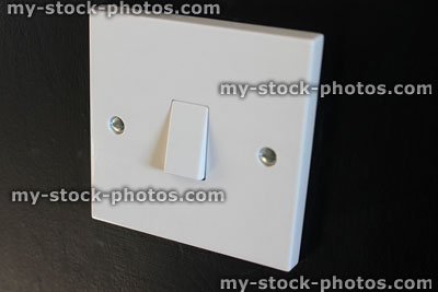 Stock image of white plastic, square single light switch, black wall