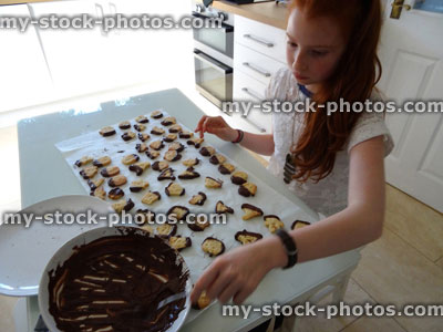 Stock image of girl making Halloween cookies / biscuits, icing with chocolate