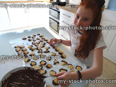 Stock image of girl making Halloween cookies / biscuits, icing with chocolate