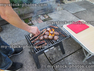 Stock image of man cooking sausages and burgers on barbecue / bbq