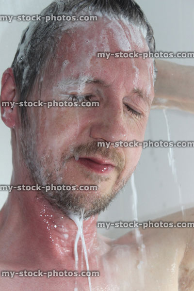 Stock image of young man with beard taking a shower, washing hair, shampoo