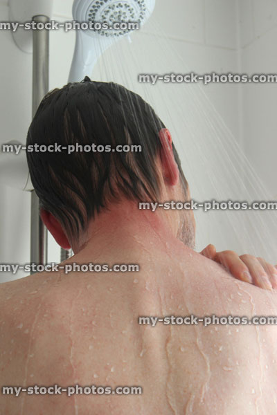 Stock image of young man taking a shower, washing his back and shoulders
