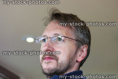 Stock image of man with short hair, beard, rimless glasses, looking out window