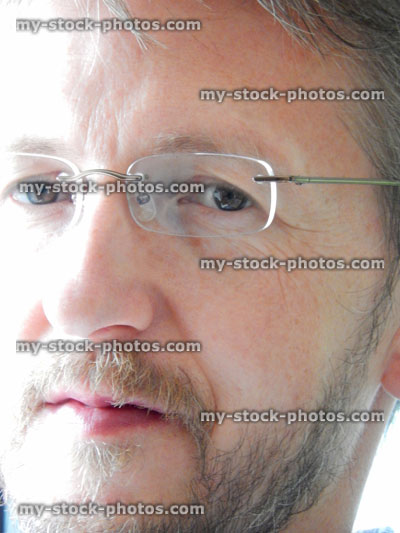 Stock image of man with short hair, beard, rimless glasses, looking stern, cross