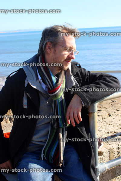 Stock image of man sitting on beach wearing winter coat / scarf