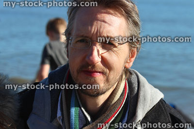 Stock image of man on winter beach with scarf, hoodie, rimless glasses