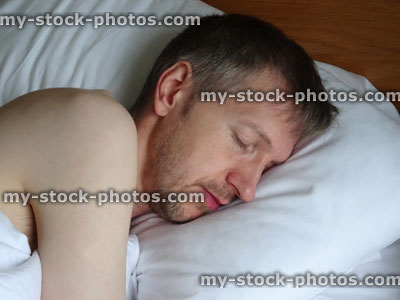 Stock image of naked man asleep in bed, sleeping, snoring, stubble beard