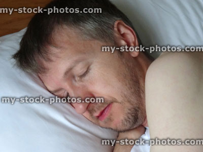 Stock image of naked man asleep in bed, sleeping, snoring, stubble beard