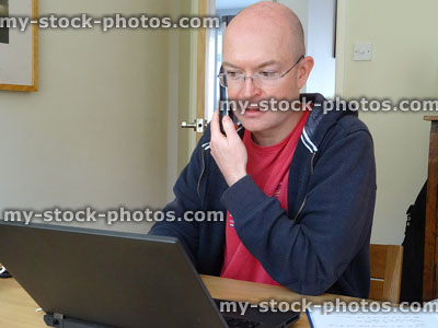 Stock image of man working at home, using phone / laptop keyboard