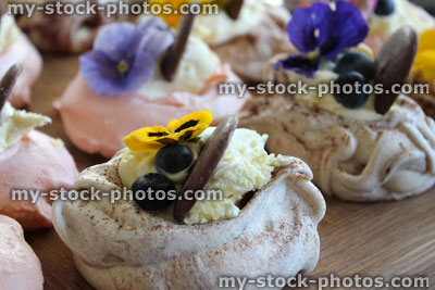 Stock image of homemade pink meringues decorated with cream, chocolate, fruit, edible flowers
