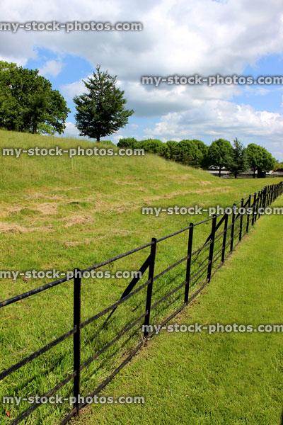 Stock image of thin black metal fence by countryside field, iron fencing