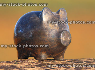 Stock image of tarnished metal piggy bank pig on stone wall, blurred background