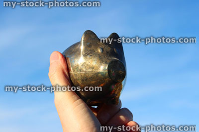 Stock image of silver metal piggy bank pig, being held / palm hand, blue sky
