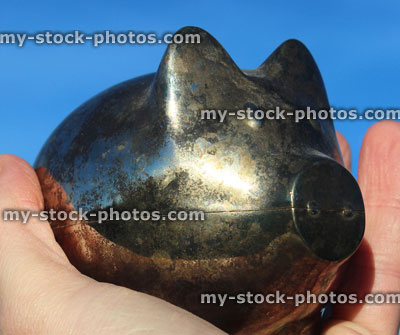 Stock image of silver metal piggy bank pig, being held / palm hand, blue sky