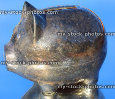 Stock image of silver metal piggy bank pig, reflection / reflectiing mirror, blue sky background