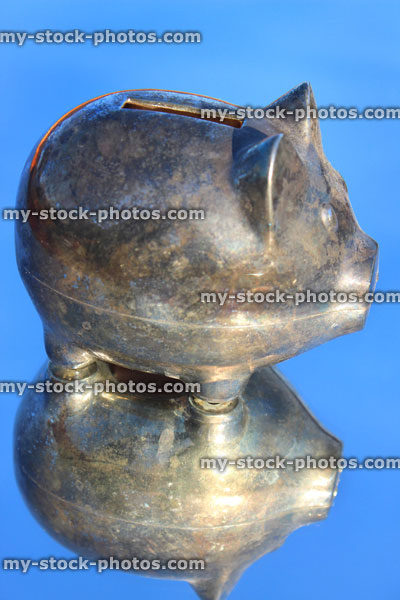 Stock image of silver metal piggy bank pig, reflection / reflectiing mirror, blue sky background