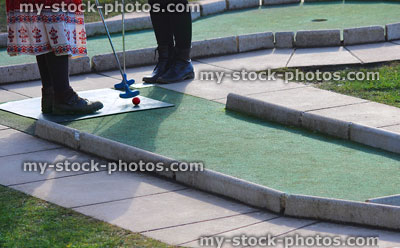 Stock image of girls hitting ball on miniature golf course putting green