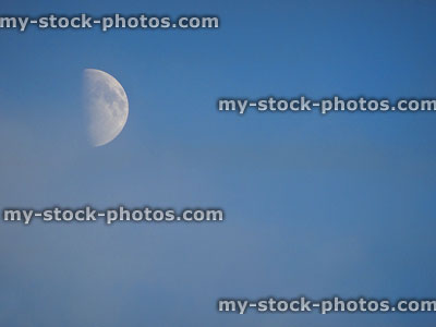 Stock image of white half moon in afternoon clear blue sky